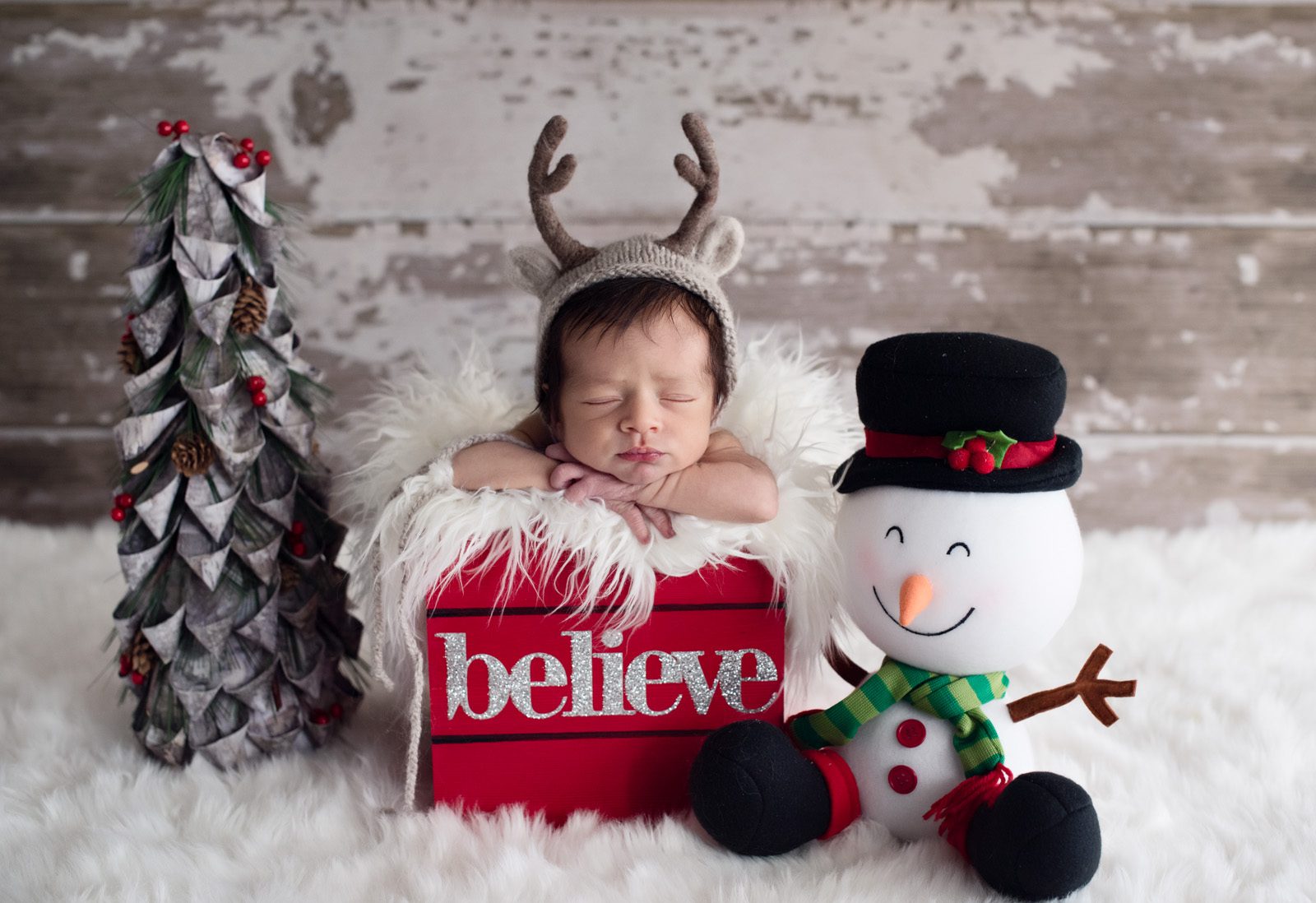 Newborn baby in a winter setting with a reindeer hat and in a wood crate that reads believe