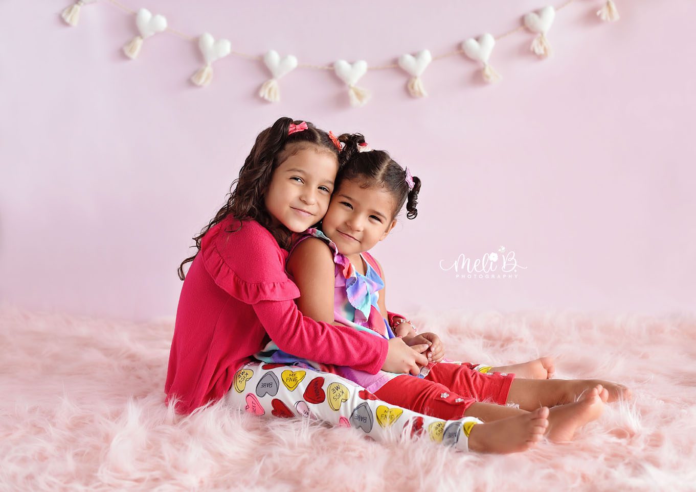 Two sisters in hugging and sitting on a pink rug