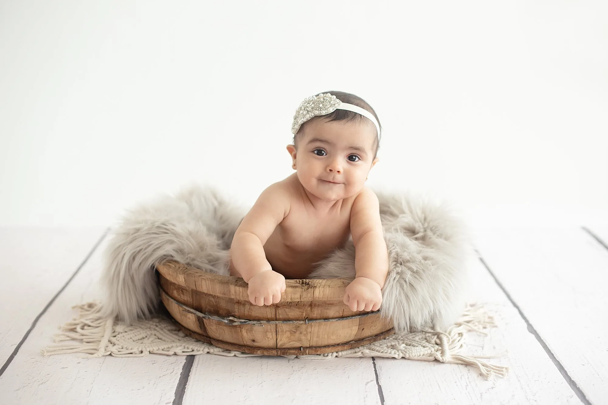 A baby girl sitting in a wooden basket.