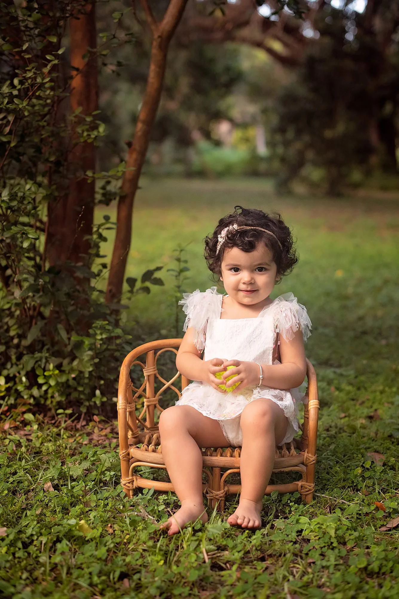 A little girl sitting in a wicker chair at outdoor Miami Children's photography session.