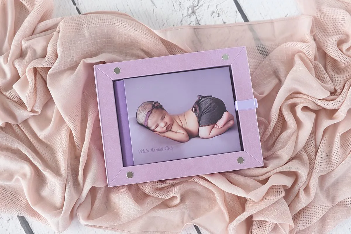 A purple baby album displayed in a frame by Miami newborn photographer MeliB