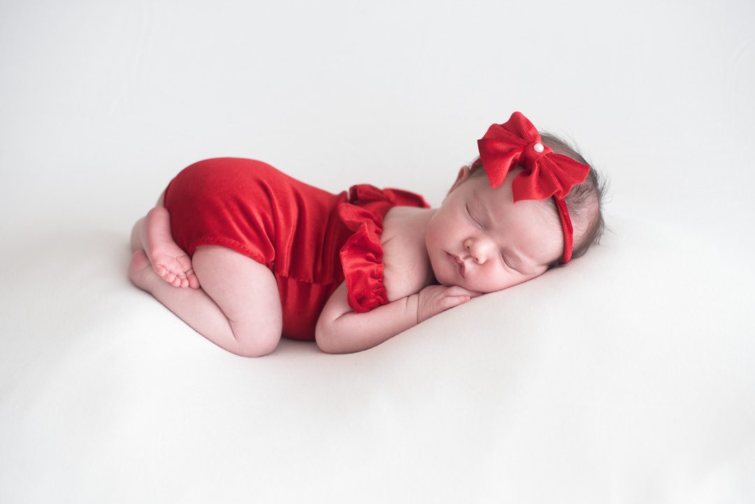 Sleeping baby in red outfit with bow by South Florida Newborn Photographer