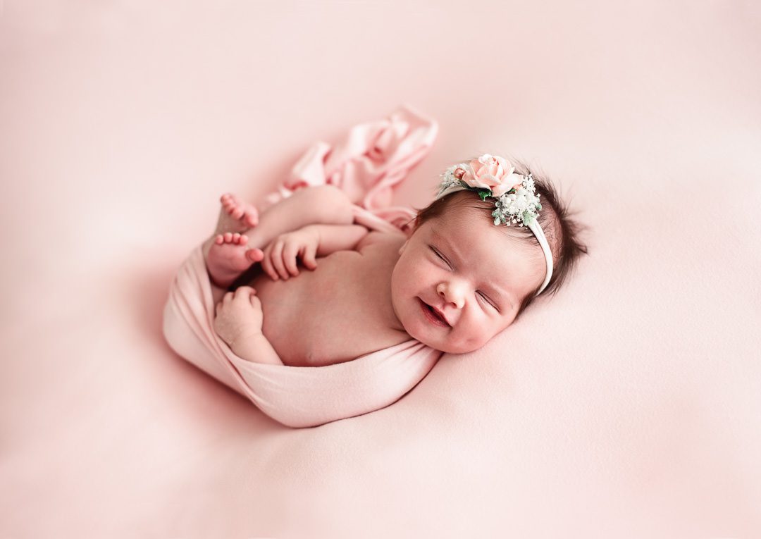 South Florida Newborn Photo of smiling baby girl wrapped in pink with floral headband