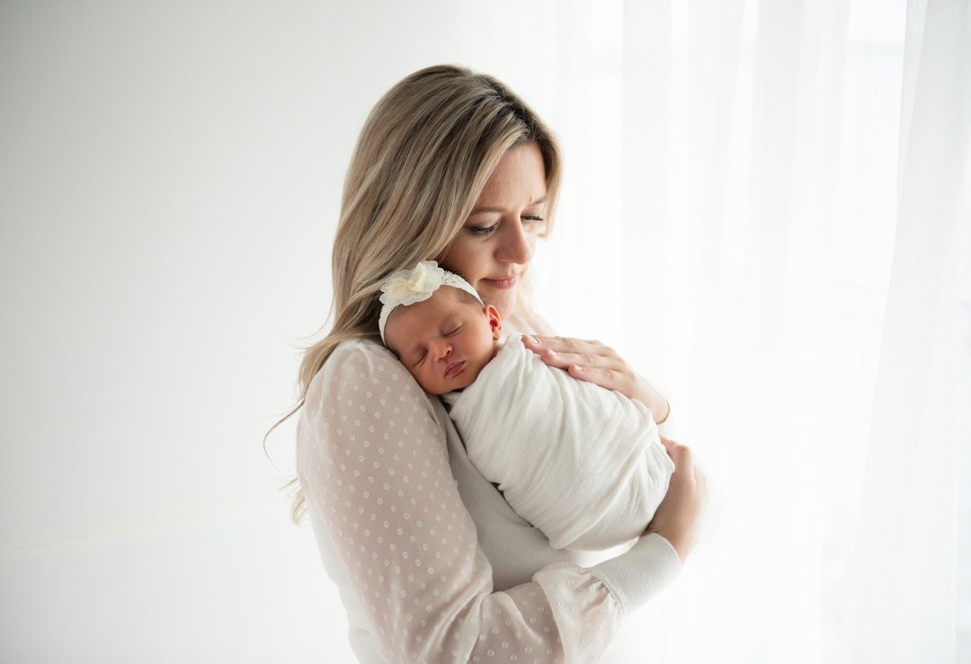 Mom holding baby in front of white backdrop for South Florida Newborn Photography session