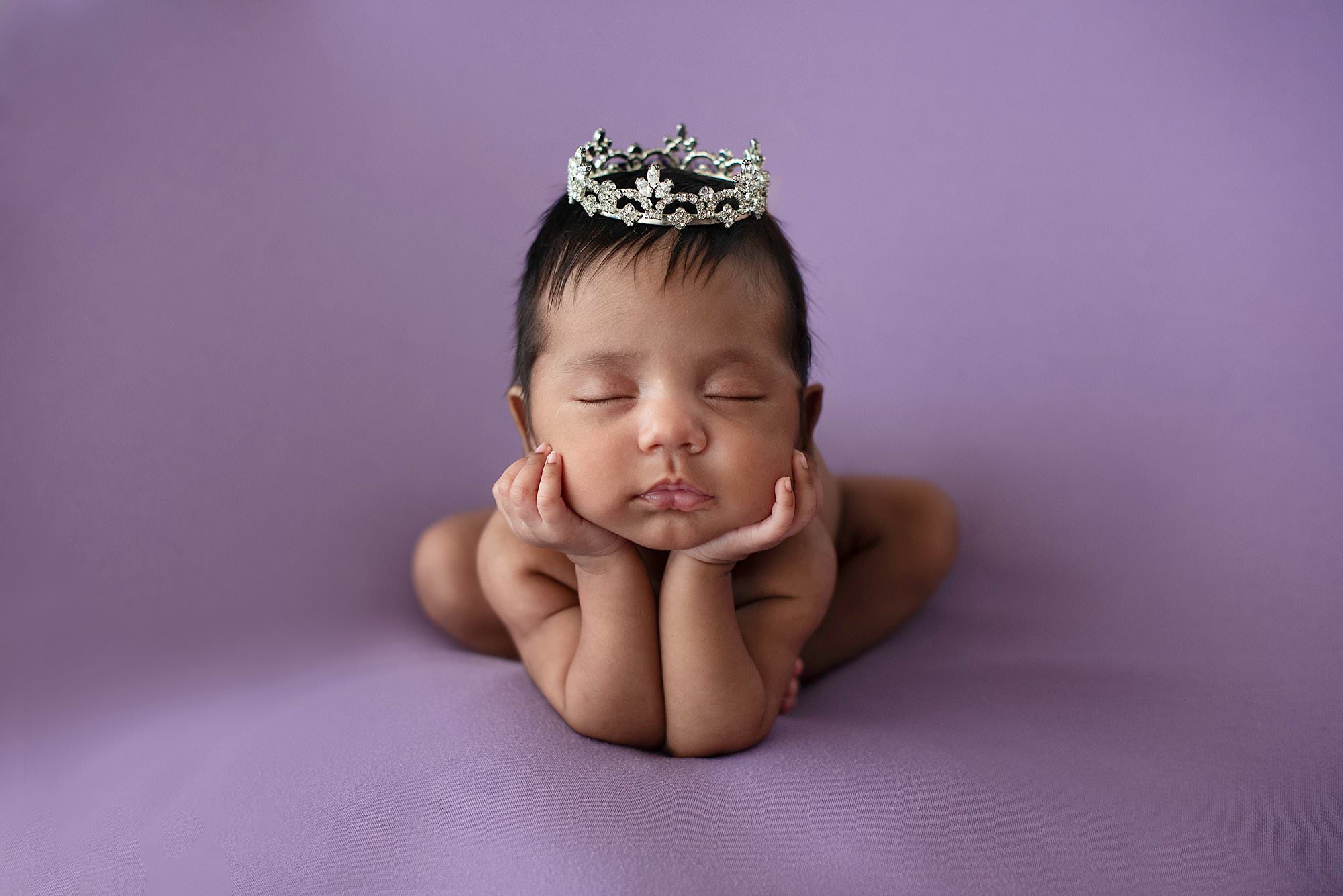 Sleeping baby wearing a crown on purple backdrop by South Florida Newborn Photographer