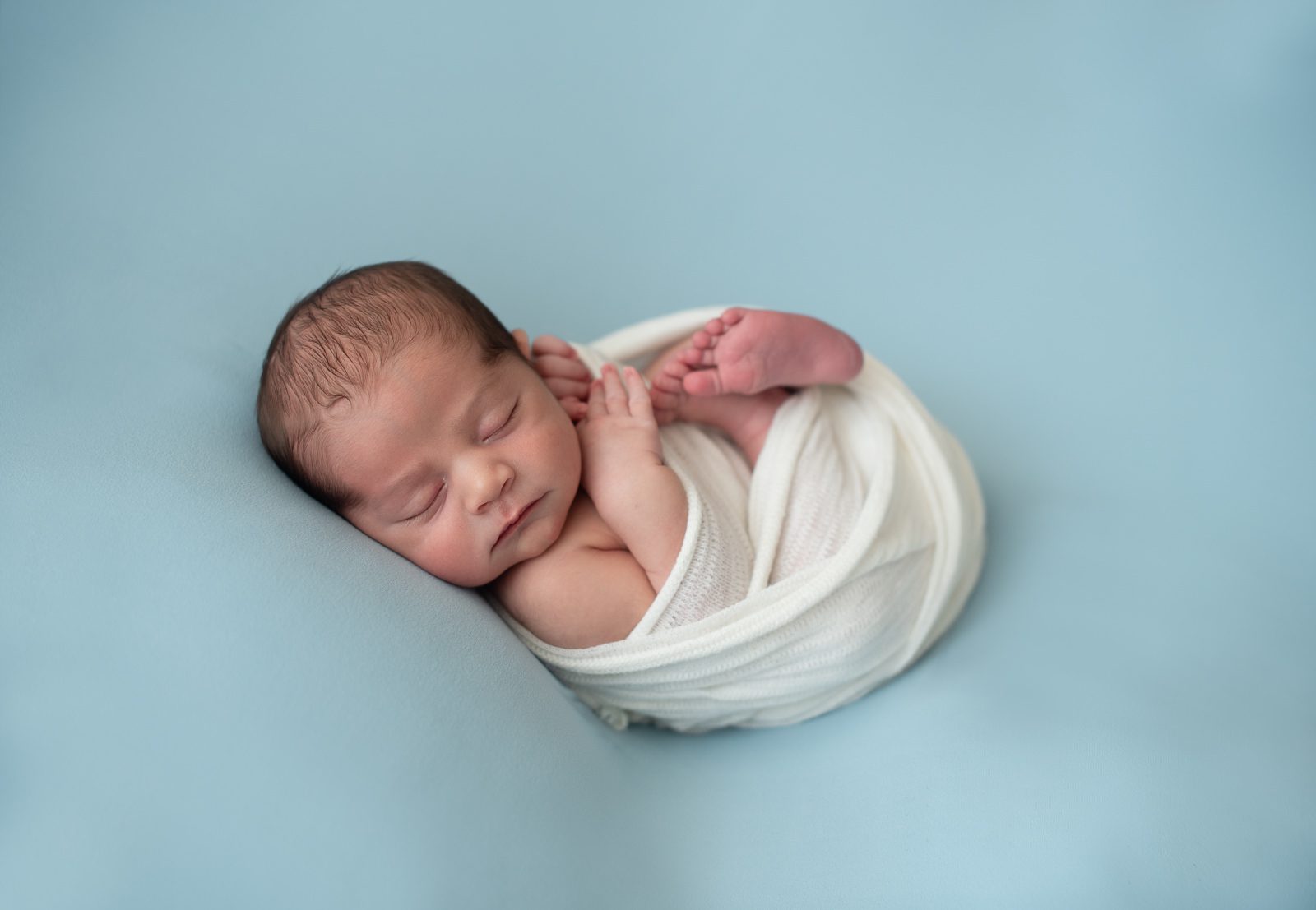 Baby swaddled in white on teal backdrop by South Florida Newborn Photographer